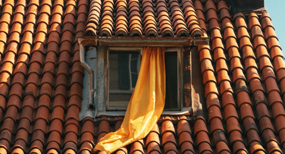 a window with a yellow curtain on a red tiled roof
